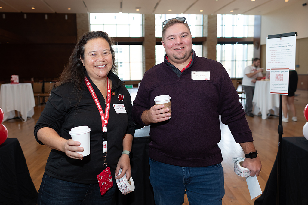 UW–Madison School of Pharmacy 2024 Alumni Tailgate and Watch Party Julie Bartell and Tyler Prickette smile for a photo with raffle tickets and coffee in their hands