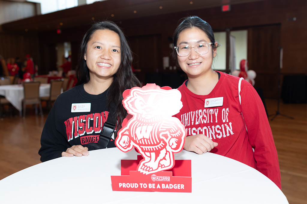 UW–Madison School of Pharmacy 2024 Alumni Tailgate and Watch Party PharmD students Soua Yang and Laurensia Tedjakusuma smile for a photo while standing at a table with a Bucky decoration