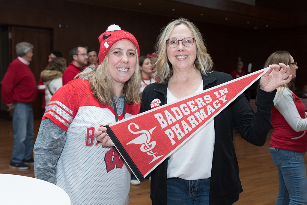 School of Pharmacy Alumni Tailgate Party 2023 Alumni smiling for camera with one holding flag that says "Badgers in Pharmacy"