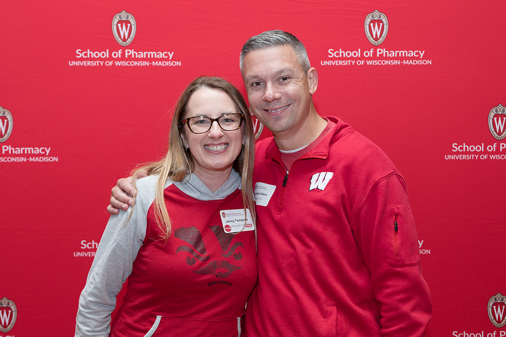 School of Pharmacy Alumni Tailgate Party 2023 Alumni smiling in front of red School of Pharmacy backdrop