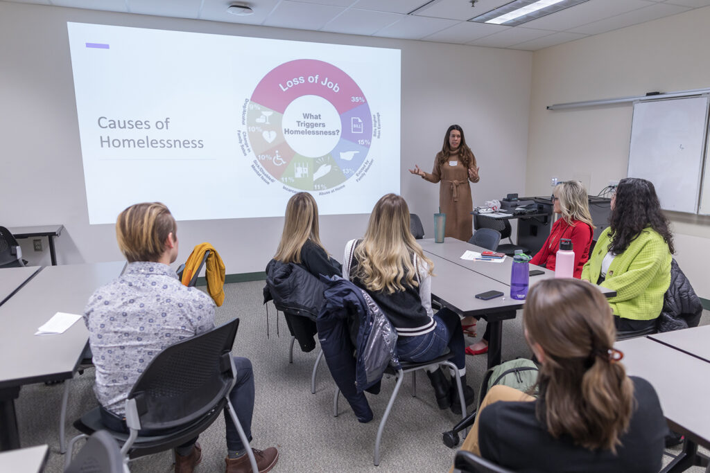 SoP Lecture: Cultivating Belonging in Pharmacy (December 1, 2023) Amy Parins speaks in front of tables of students