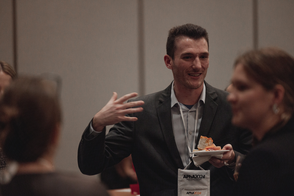 pharma0326_ A man holding a plate of food gestures while talking