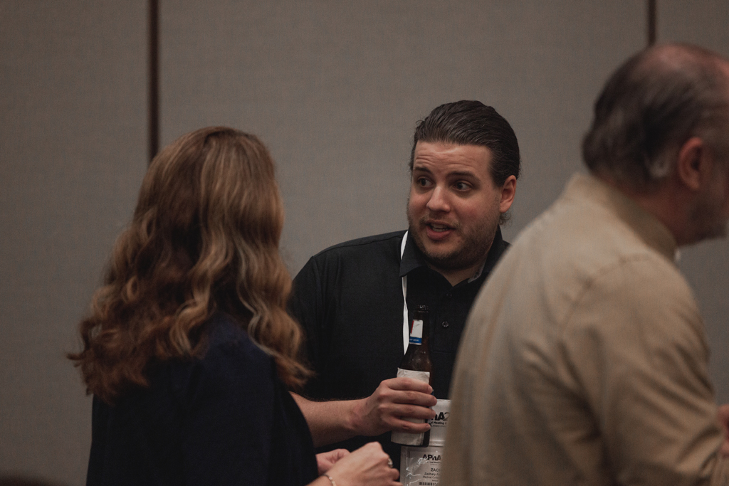 pharma0516_ A man with drink speaks with others