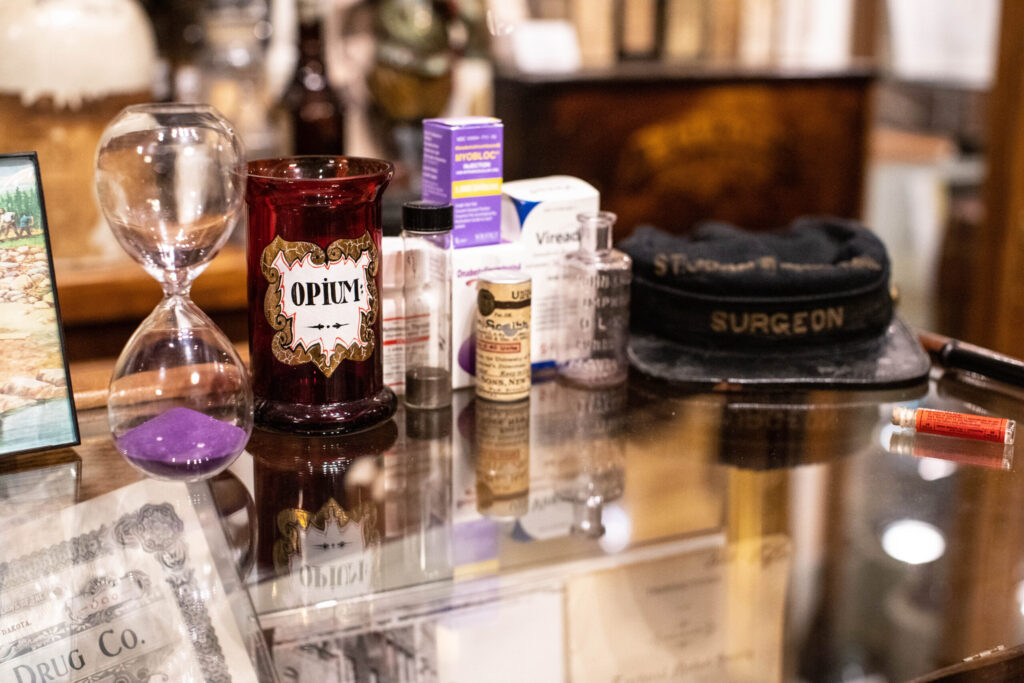 real-life-photographs-36 An old surgeon hat, a glass jar labeled "Opium," an hour glass with purple sad, and other assorted bottles.