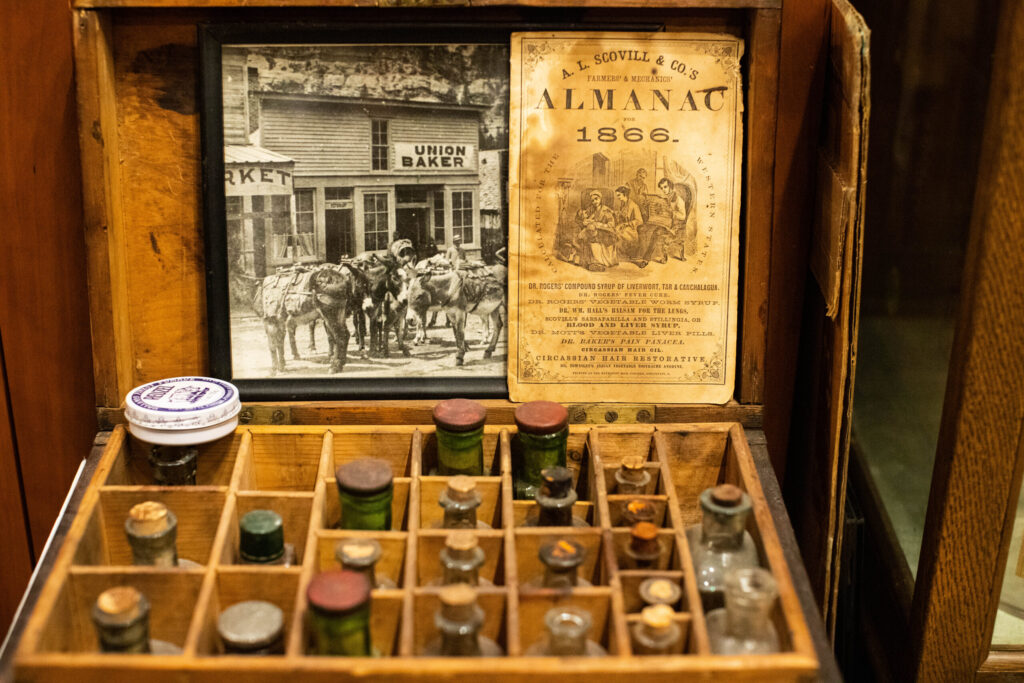 real-life-photographs-37 A wooden box filled with old glass prescription bottles, the cover of a, 1866 Almanac, and a black-and-white photo of donkeys outside of a shop called "Union Baker."