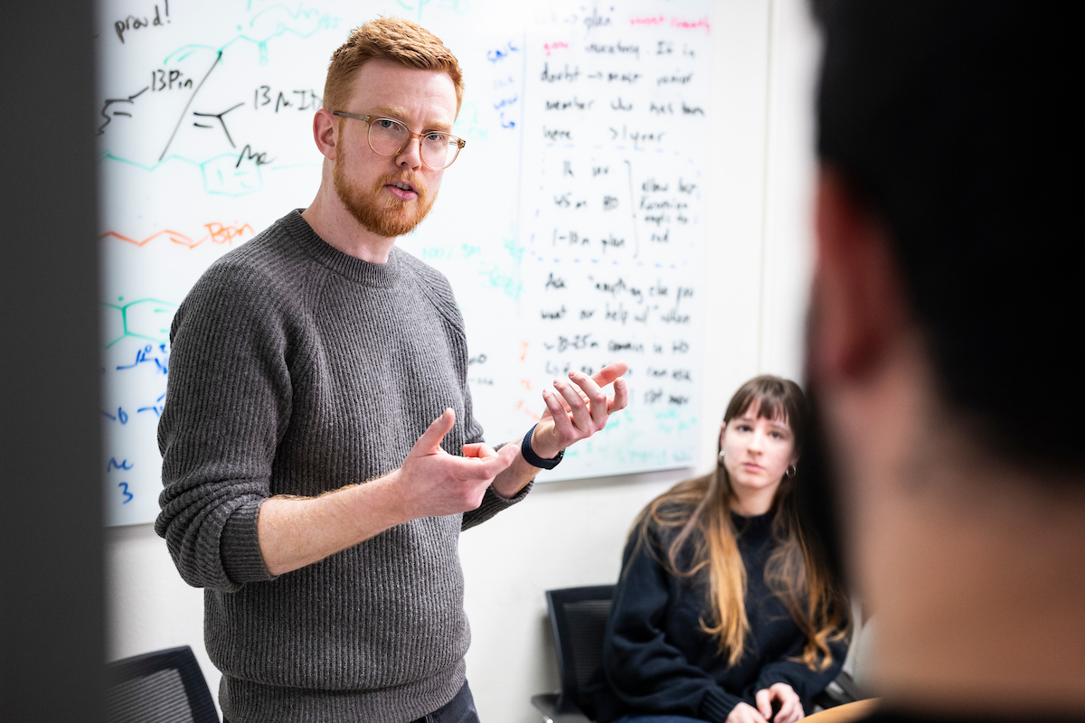 A professor standing in front of a white board discusses a concept with students