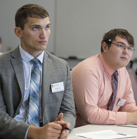 Two PharmD-MBA students sit at a table together, listening to a guest speaker presentation